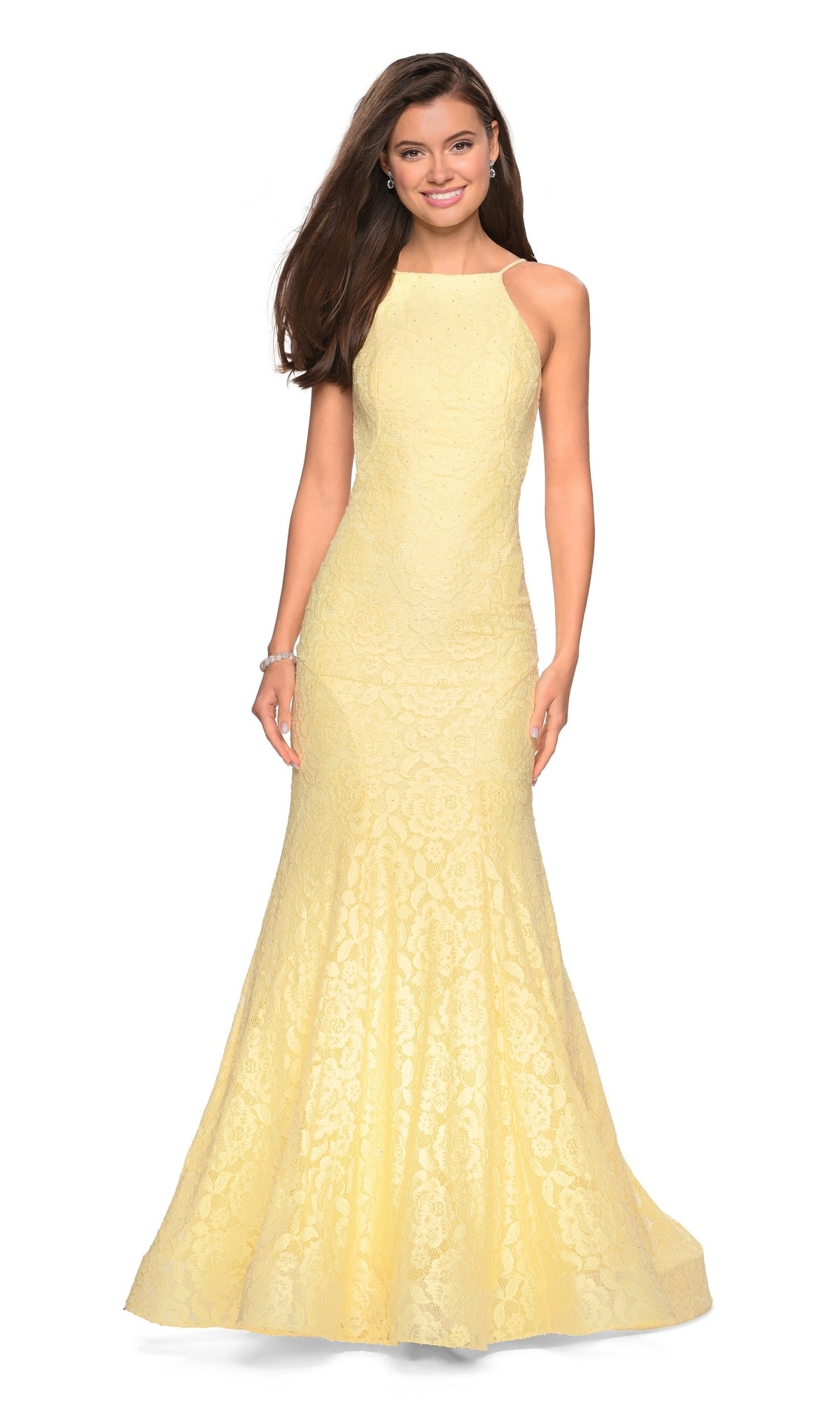 Woman wearing the La Femme Floral Lace Mermaid Prom Dress 27289—a sleeveless, floor-length pale yellow gown with floral lace and a high neckline—standing and smiling with her hands by her sides.
